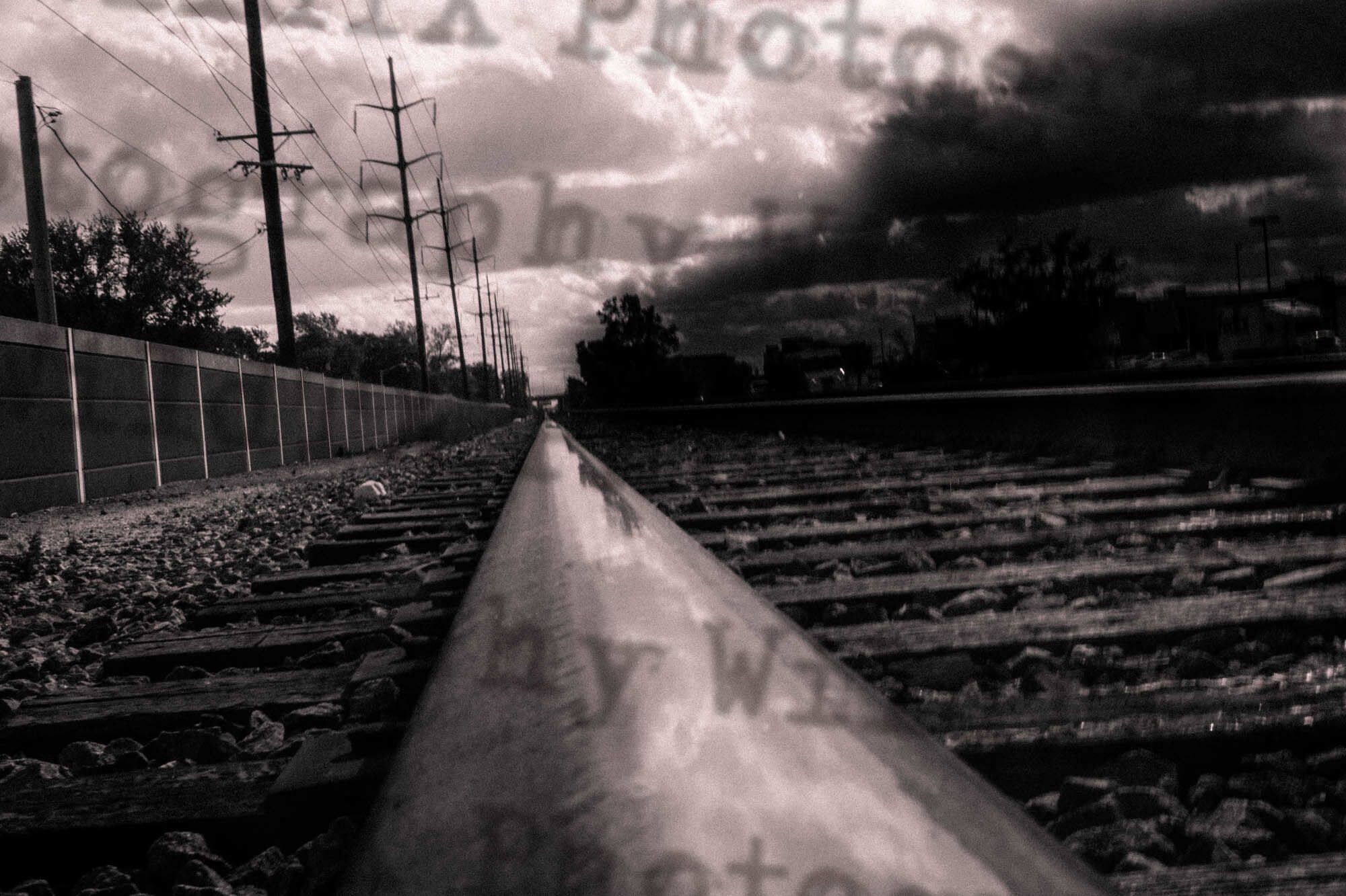 Black and white photo of railroad tracks receding into the distance under a stormy dramatic sky